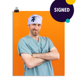 Photo of a man in seafoam colored scrubs and a light purple head wrap with an embroidered hand holding a drill. His arms are crossed as he leans to his right and smirks at the viewer. On an orange colored background. This print is signed by the doctor!