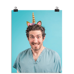 Photo of a man with an almost manic looking smile as he wears seafoam colored scrubs and a glittering gold unicorn horn headband on his head. On a seafoam colored background.