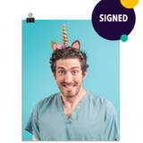 Photo of a man with an almost manic looking smile as he wears seafoam colored scrubs and a glittering gold unicorn horn headband on his head. On a seafoam colored background.This print is signed by the doctor!