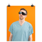 Photo of a man wearing large black glasses and seafoam colored scrubs looking up to the left. On an orange background.