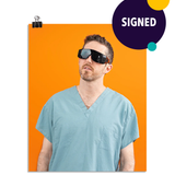 Photo of a man wearing large black glasses and seafoam colored scrubs looking up to the left. On an orange background. This print is signed by the doctor!