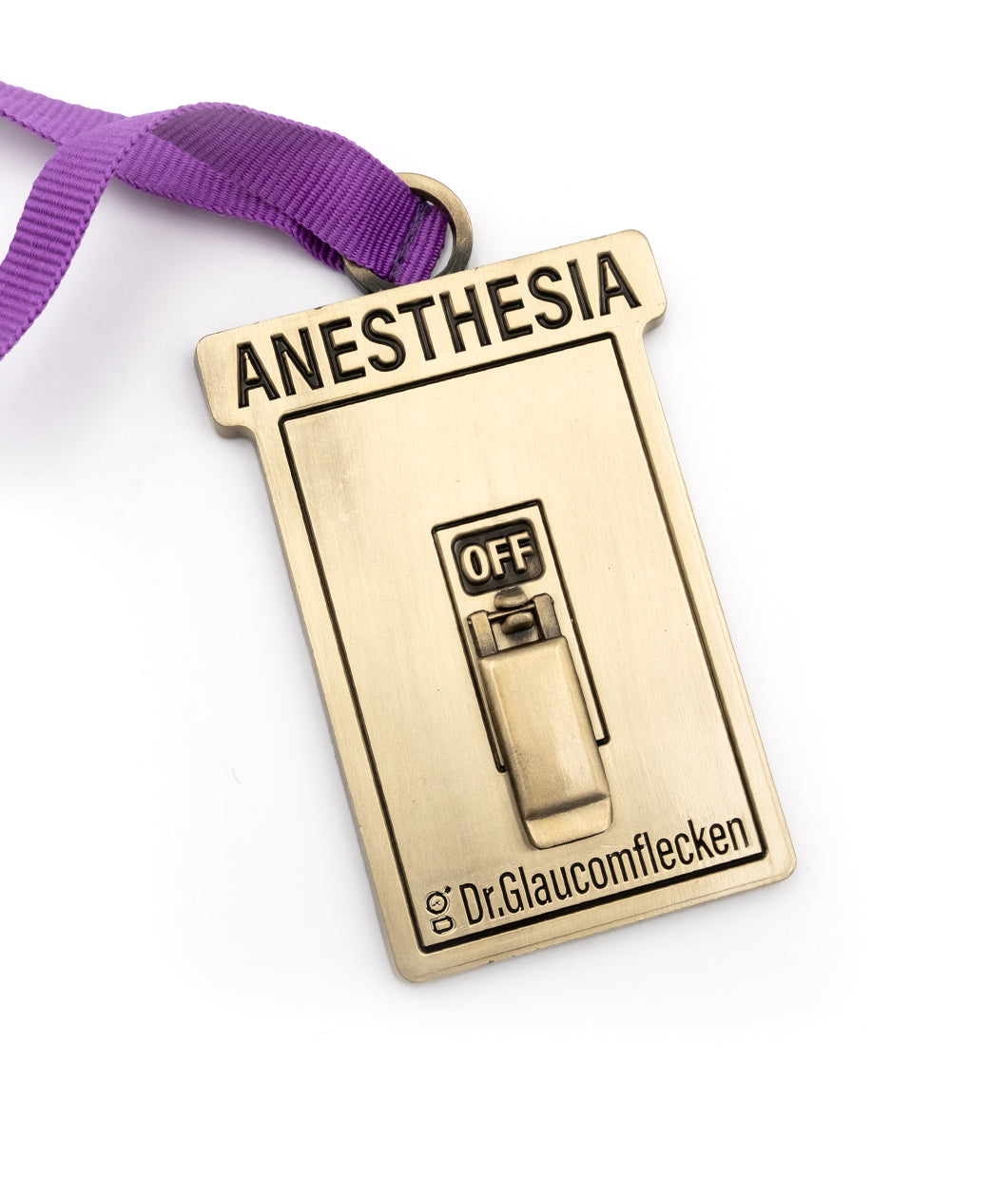 Gold metal rectangular ornament that says Anesthesia on the top, recessed into the metal, and then a 3D switch can flip up or down to indicate ON or OFF in the middle. The bottom has Dr.Glaucomflecken recessed into the metal. A ribbed purple ribbon is attached at the top so it can hang on a tree.