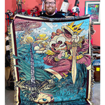 Jesse Cox a red bearded bespectacled man holding the blanket bearing his likeness in cartoon form. 