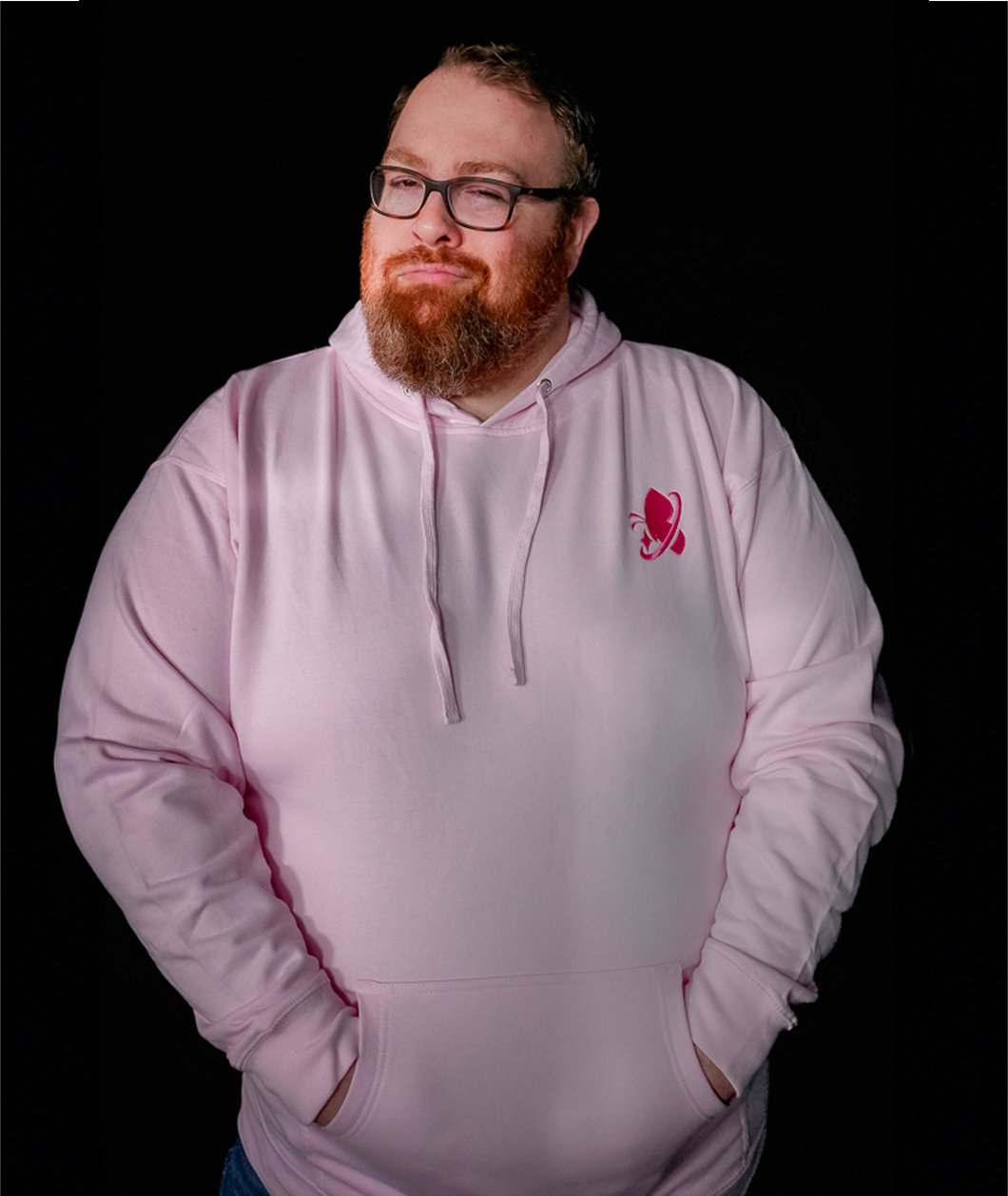 Jesse Cox, a burly man with a big red beard winking at the camera wearing his light pink hoodie with a pink embroidered space butterfly logo in the right chest area.