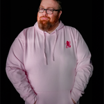 Jesse Cox, a burly man with a big red beard winking at the camera wearing his light pink hoodie with a pink embroidered space butterfly logo in the right chest area.