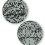 A digital mockup of a dark silver coin. The front shows an image of a bus with the text "One DBloon; Agimus Liberos Adjutum" The back shows an image of a road and tree-shaped air freshener with the text "Desert Bus for Hope 2023"