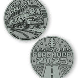 A digital mockup of a dark silver coin. The front shows an image of a bus with the text "One DBloon; Agimus Liberos Adjutum" The back shows an image of a road and tree-shaped air freshener with the text "Desert Bus for Hope 2025"