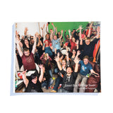 A photo of the front of the Desert Bus for Hope Seven photo book. It features a group of people from Desert Bus raising their hands in celebration.