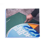 A photo of the front of the Desert Bus for Hope 2022 photo book. It features a hand trimming the margin off of a Desert Bus for Hope 2022 sign.