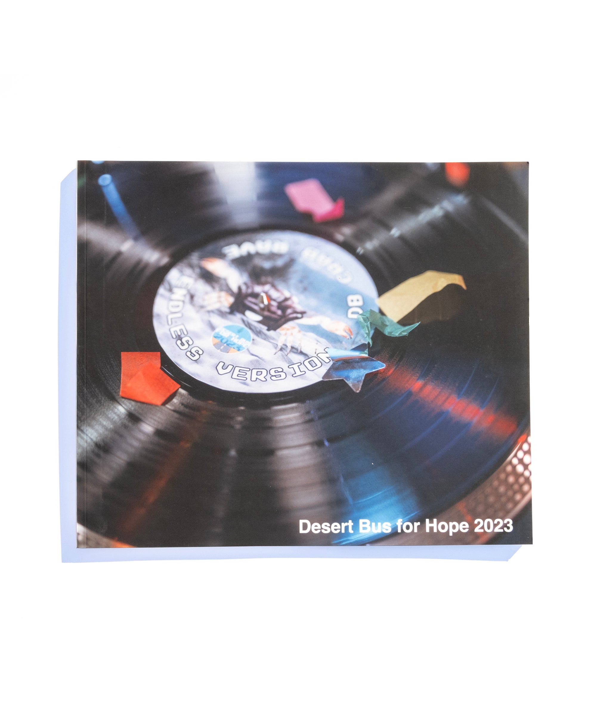 A photo of the front of the Desert Bus for Hope 2023 photo book. It features a vinyl record with confetti fallen over it.