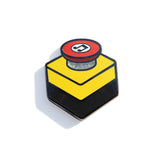 A photo of an enamel pin designed to resemble an emergency stop button. 