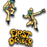 Three enamel pins, one that reads "First of October" in bubbly letters, one of a person wearing a suit and holding a cup with an "R" on it and one of a person in a suit with a top hat holding a cup with an "A" on it. 