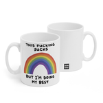 Two white mugs sitting next to each other showing two sides of the same mug. The front side has text that reads "This fucking sucks; but I'm doing my best". In between the two lines of text is a rainbow. On the back of the mug is a small black square with the words "Semi Rad".