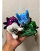 A hand holding three of the bug plushies from Tyler Thrasher. One is white with purple sequins, one is blue with blue sequins and one is green with green sequins. 