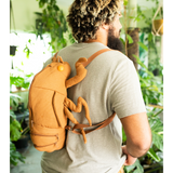 Man wearing cicada shell shaped backpack in a room full of plants. Looks like a giant cicada crawling up his back.