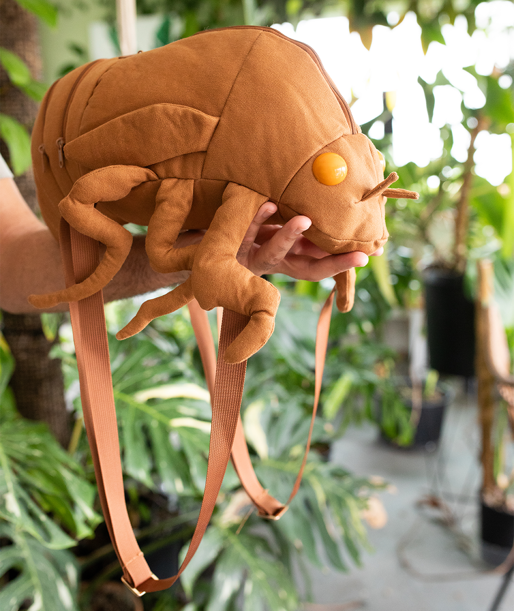 Man holding cicada shell shaped backpack. Backpack takes up his whole forearm as he holds the head of the bag in his hand.