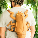 Man wearing cicada shell shaped backpack in very sunny lighting in a room with many plants.