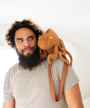 Man looking puzzled at a cicada shell shaped backpack resting on his shoulder like a parrot. Clearly a personality pic.