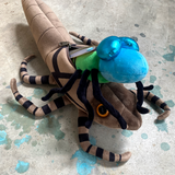 Bright blue dragonfly plush emerging from its larve taupe colored plush shell.