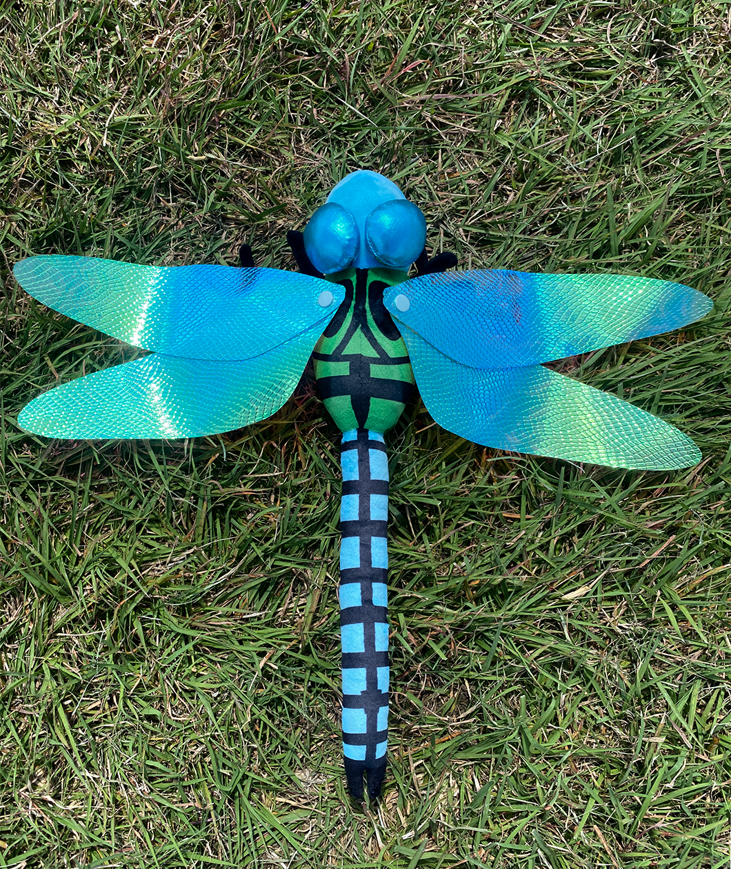 Bright blue dragonfly plush with iridescent wings outstretched attached to a green body with black markings.