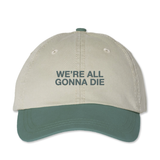 Khaki colored dad hat with sage green brim and embroidery that is front and centered and says in bold uppercase font, "WE'RE ALL GONNA DIE"