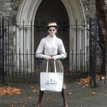 A photograph of Bernadette posing holding the Menace to Polite Society Tote Bag in front of her legs.