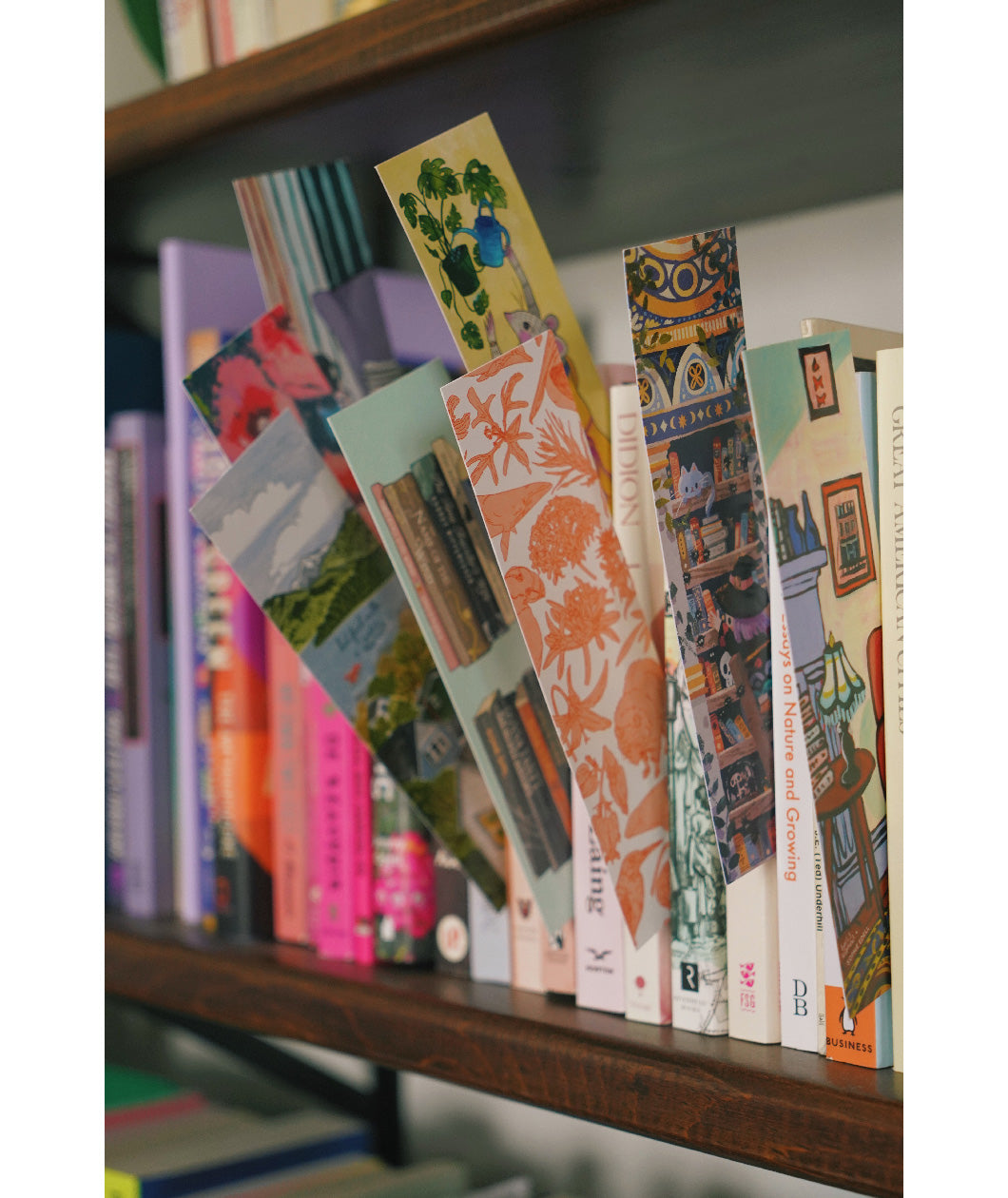 Paper bookmarks with fun designs displayed by being wedged between books on a shelf. From Books Unbound.