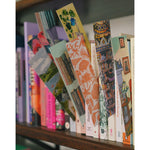 Paper bookmarks with fun designs displayed by being wedged between books on a shelf. From Books Unbound.