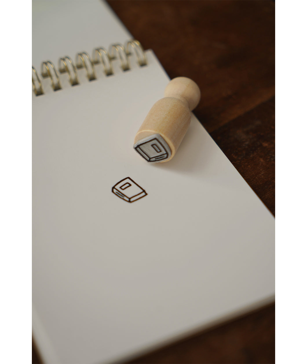 A photo of a miniature stamp of a book illustration. The stamp has been used on a fresh page of a notepad on a table. From Books Unbound.