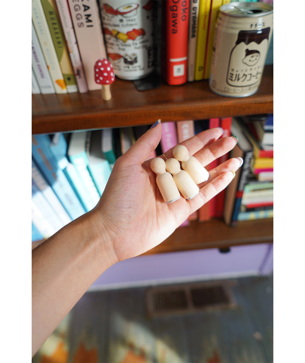 A photo of miniature stamps of a book illustration. Three stamps are held in a hand in front of a colorful bookcase. From Books Unbound.