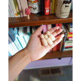 A photo of miniature stamps of a book illustration. Three stamps are held in a hand in front of a colorful bookcase. From Books Unbound.