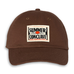 Brown hat with heat pressed woven label that says "Summer Conclave" and a sunrise that looks like an eye.
