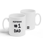A white mug with a design printed on the front and back. The front has black handwritten text that reads, "Aspiring #1 Dad" and the back has the Semi-Rad logo. From Semi-Rad.