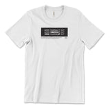 A white t-shirt with a black rectangle in the center with the words "We're figuring it out" written three times in a row with the second line has "figuring" crossed out and the third line has "we're" and "it" crossed out. There is additional small text below this. From Answer in Progress.