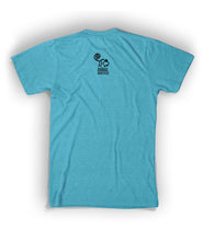 Back of blue shirt with Animal Wonders logo below collar. Logo is of black cartoon silhouette drawing of monkey with spiral tail is above “Animal Wonders INC” with each word in black, all caps, sans serif font, and varying sizes. INC is on its side at end of the word Wonders, which are below Animal - from Animal Wonders