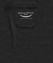 Close-up on a black pocket with the words "Dorian Smiles Inc." over a curved smile and the phrase "Why don't you join me?" in white. The phrase is repeated in undulating patterns of black ink underneath the white words. By Brian David Gilbert