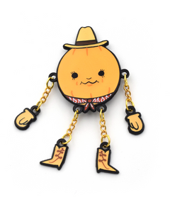 A pumpkin dressed like a cowboy, wearing a cowboy hat and a bandana. Each hand and cowboy boot is connected to the body with a small gold chain. From Brian David Gilbert.