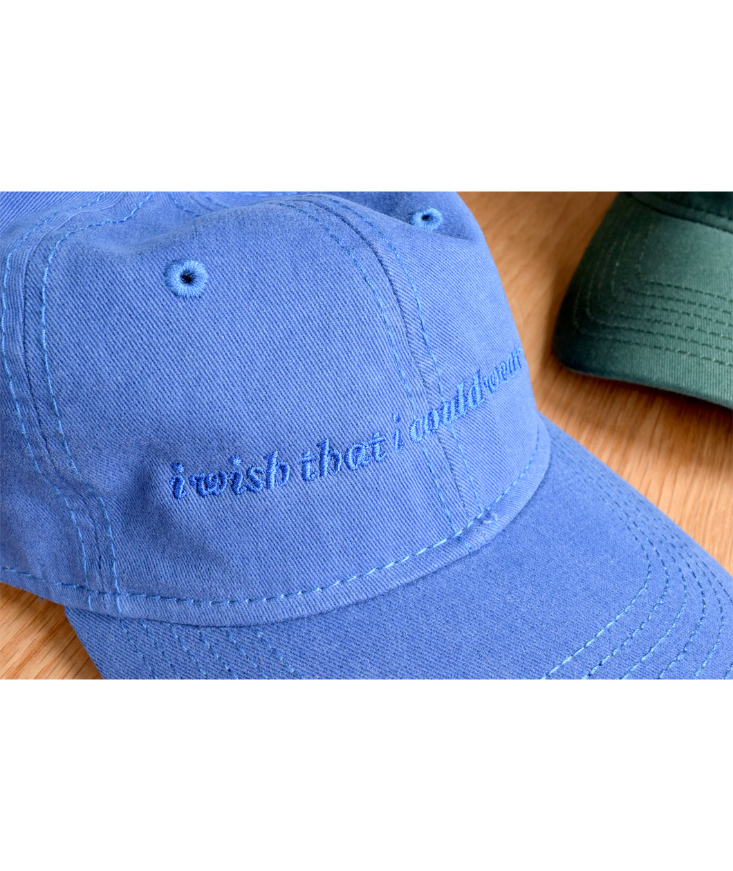 Close up of blue ball cap with lowercase embroidered words saying "i wish that i could wear hats". From Brian David Gilbert. 