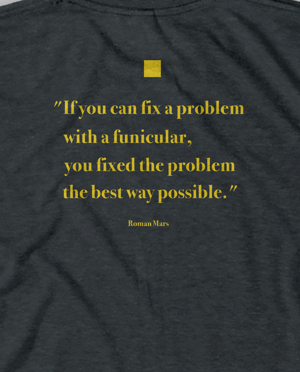 A close-up of a yellow quote on a gray shirt - by 99% Invisible