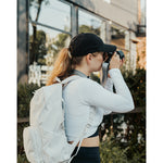 Lizzie Peirce wearing a hat, a backpack and holding a camera to her face.