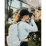 Lizzie Peirce wearing a hat, a backpack and holding a camera to her face.