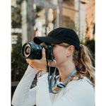 Lizzie Peirce wearing a hat and holding a camera to her face.
