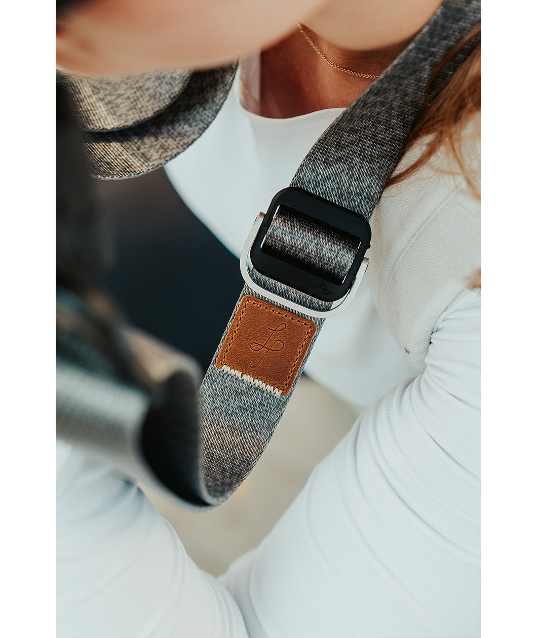 A close up of a grey camera strap with a brown leather square that has a "LP" etched into it for Lizzie Peirce.