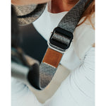 A close up of a grey camera strap with a brown leather square that has a "LP" etched into it for Lizzie Peirce.