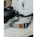 A close up of a grey camera strap attached to a camera with a brown leather square that has a "LP" etched into it for Lizzie Peirce.