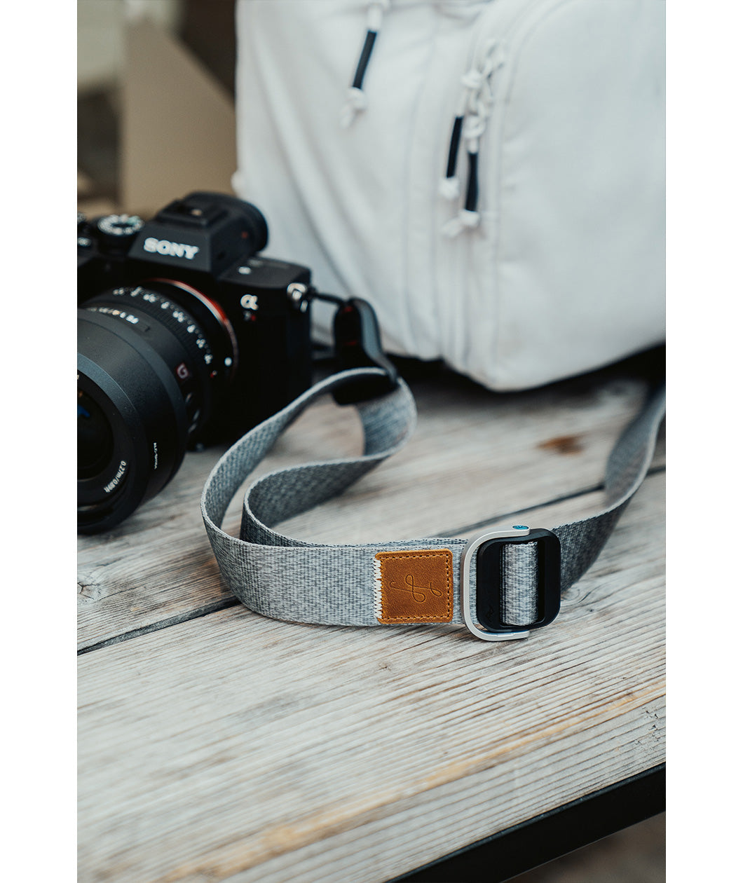 A close up of a grey camera strap attached to a camera with a brown leather square that has a "LP" etched into it for Lizzie Peirce.