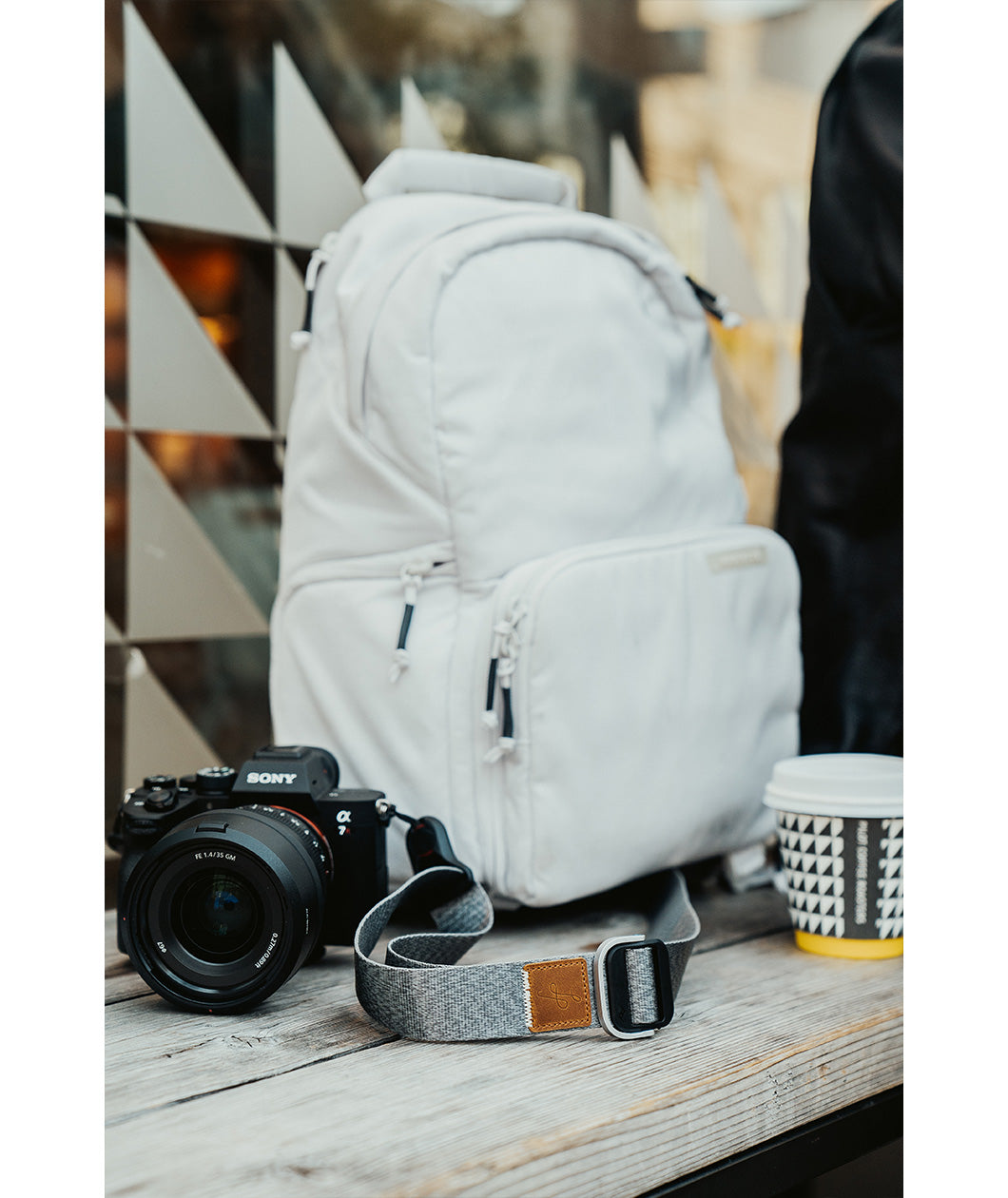 A grey camera strap attached to a camera with a brown leather square that has a "LP" etched into it for Lizzie Peirce.
