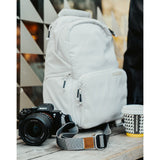 A grey camera strap attached to a camera with a brown leather square that has a "LP" etched into it for Lizzie Peirce.