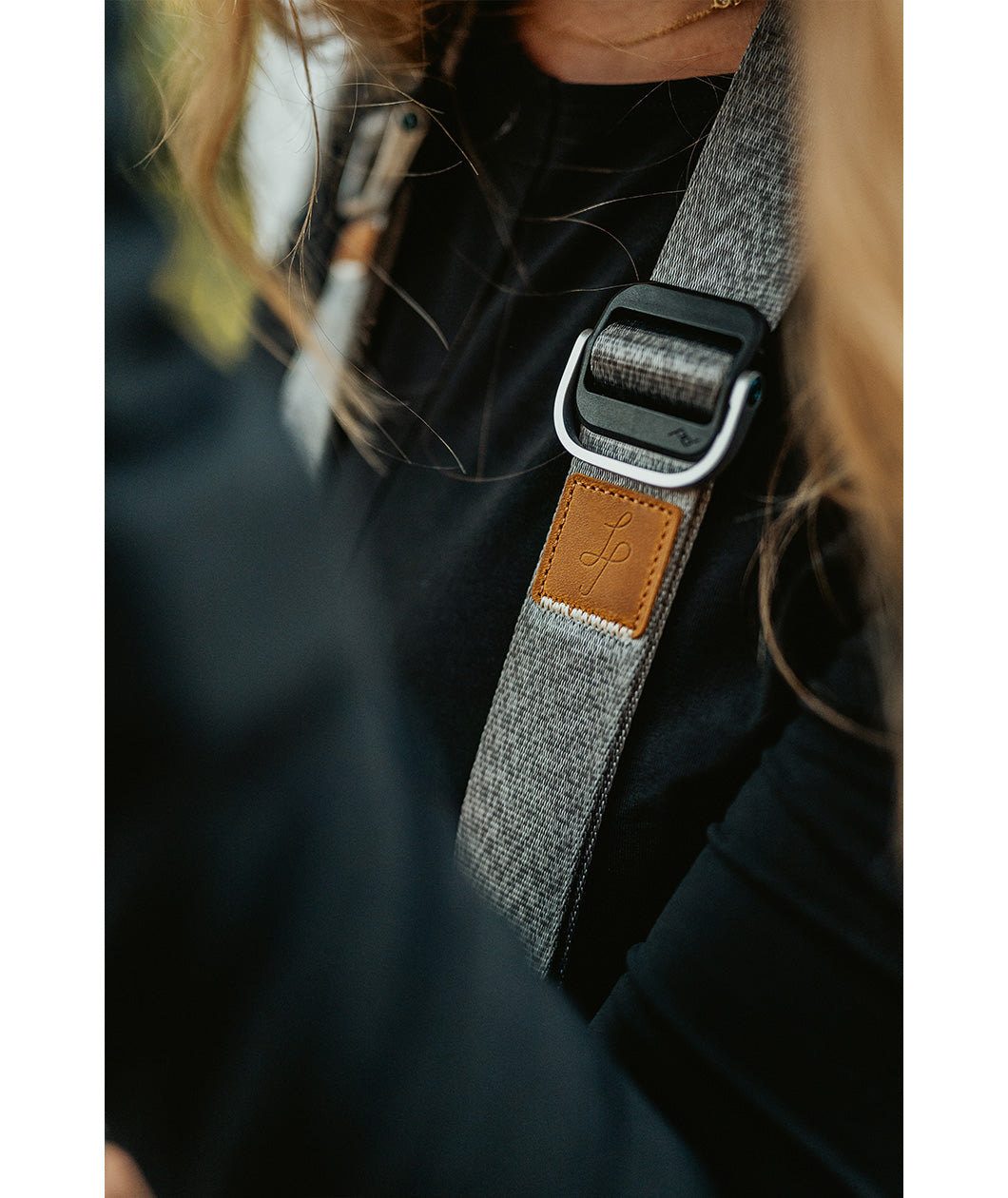 A close up of a grey camera strap with a brown leather square that has a "LP" etched into it for Lizzie Peirce.