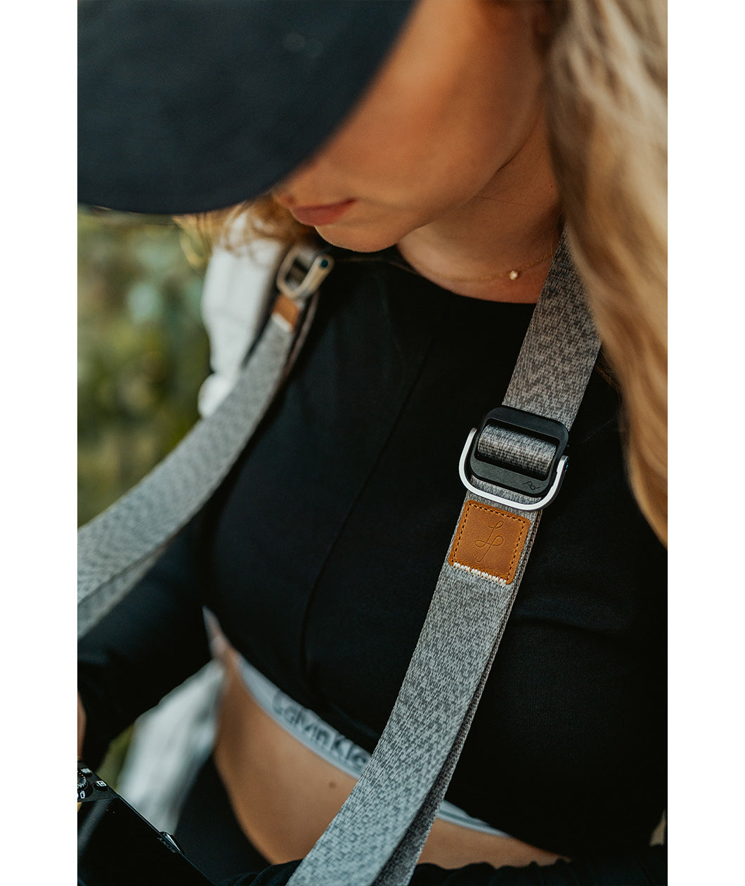A close up of a grey camera strap attached to a camera with a brown leather square that has a "LP" etched into it for Lizzie Peirce.